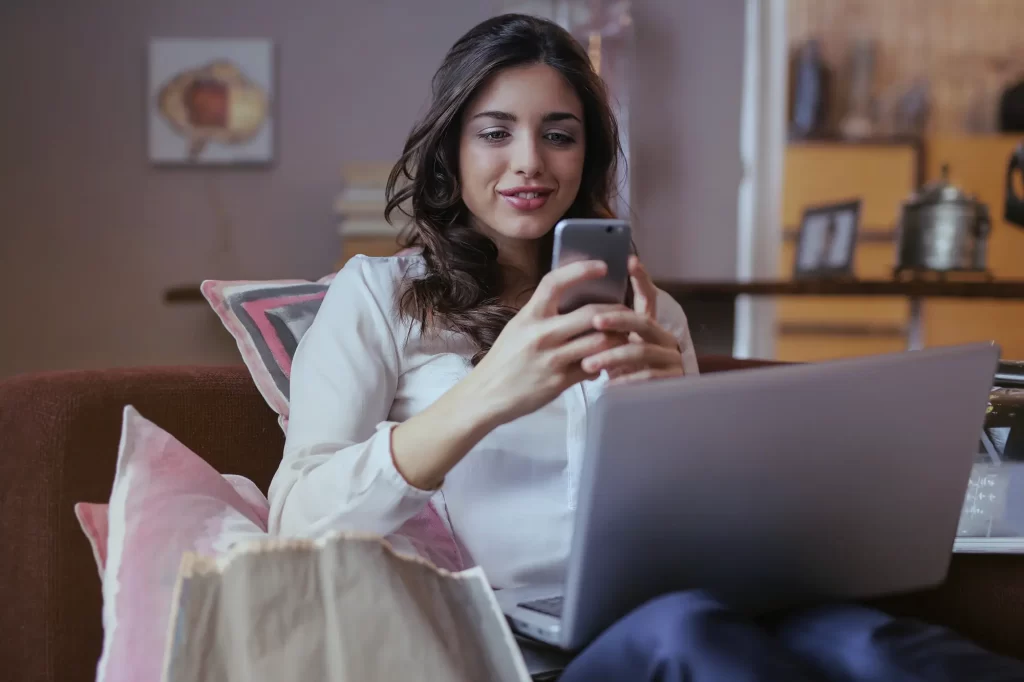 girl scrolling on her phone with her laptop