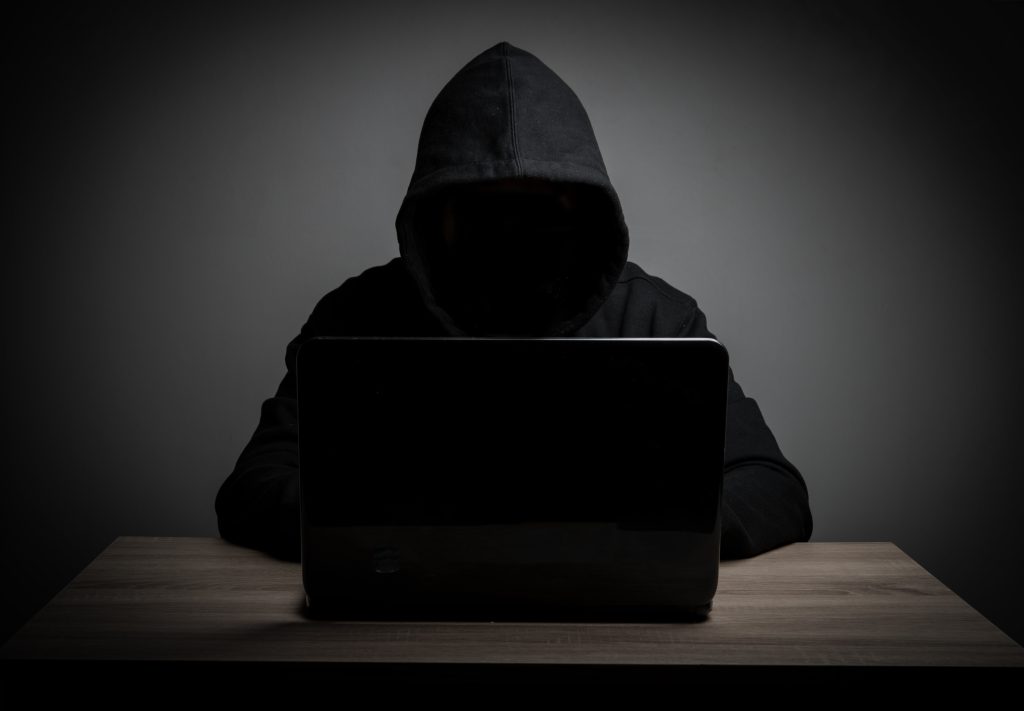 Hacker in a black hoodie working with his laptop